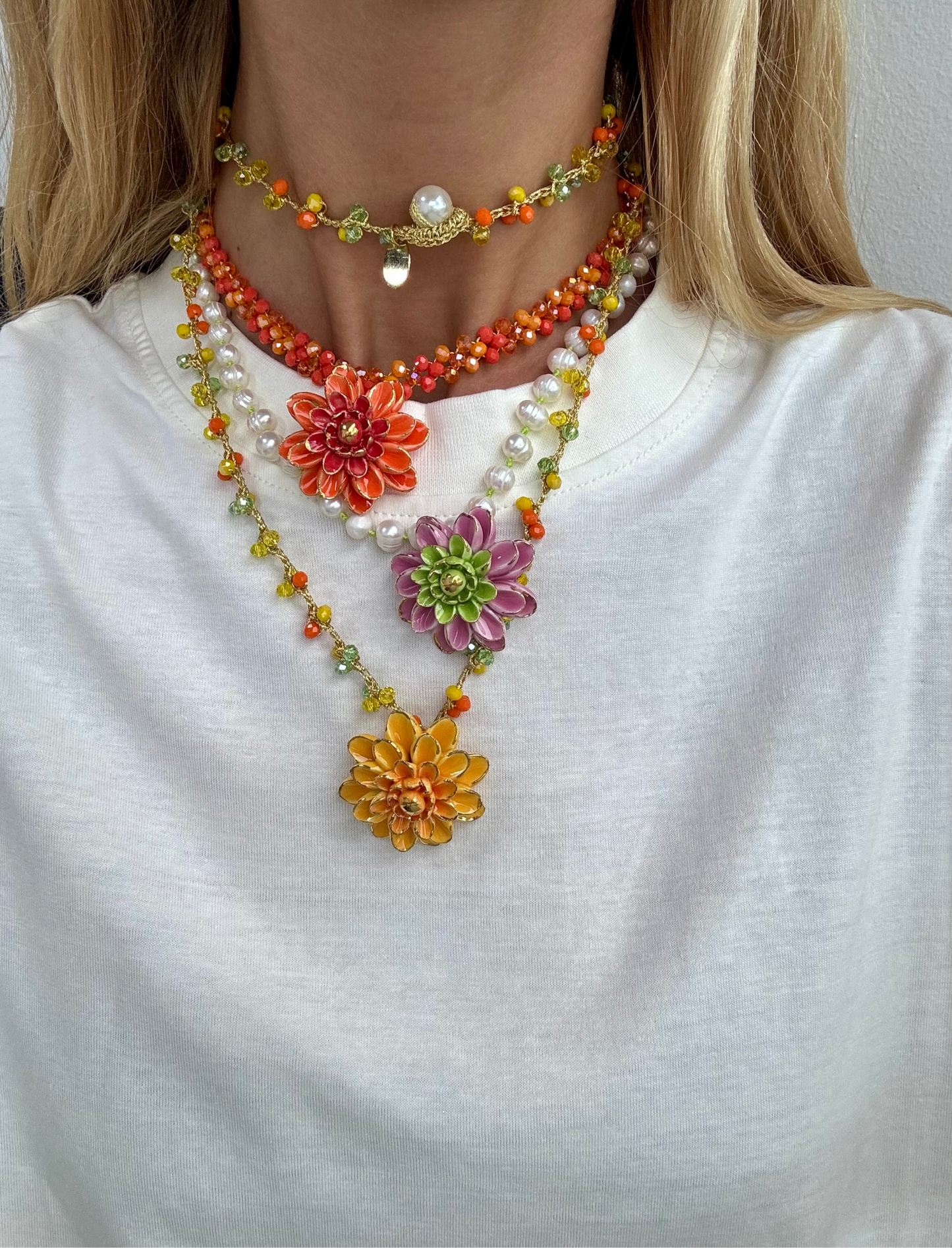Collar de cuentas facetadas en tonos naranjas con colgante central de flor esmaltada en naranja degradado, sobre fondo camiseta blanca con el collar Fiorella y Sofía. Cashfana.