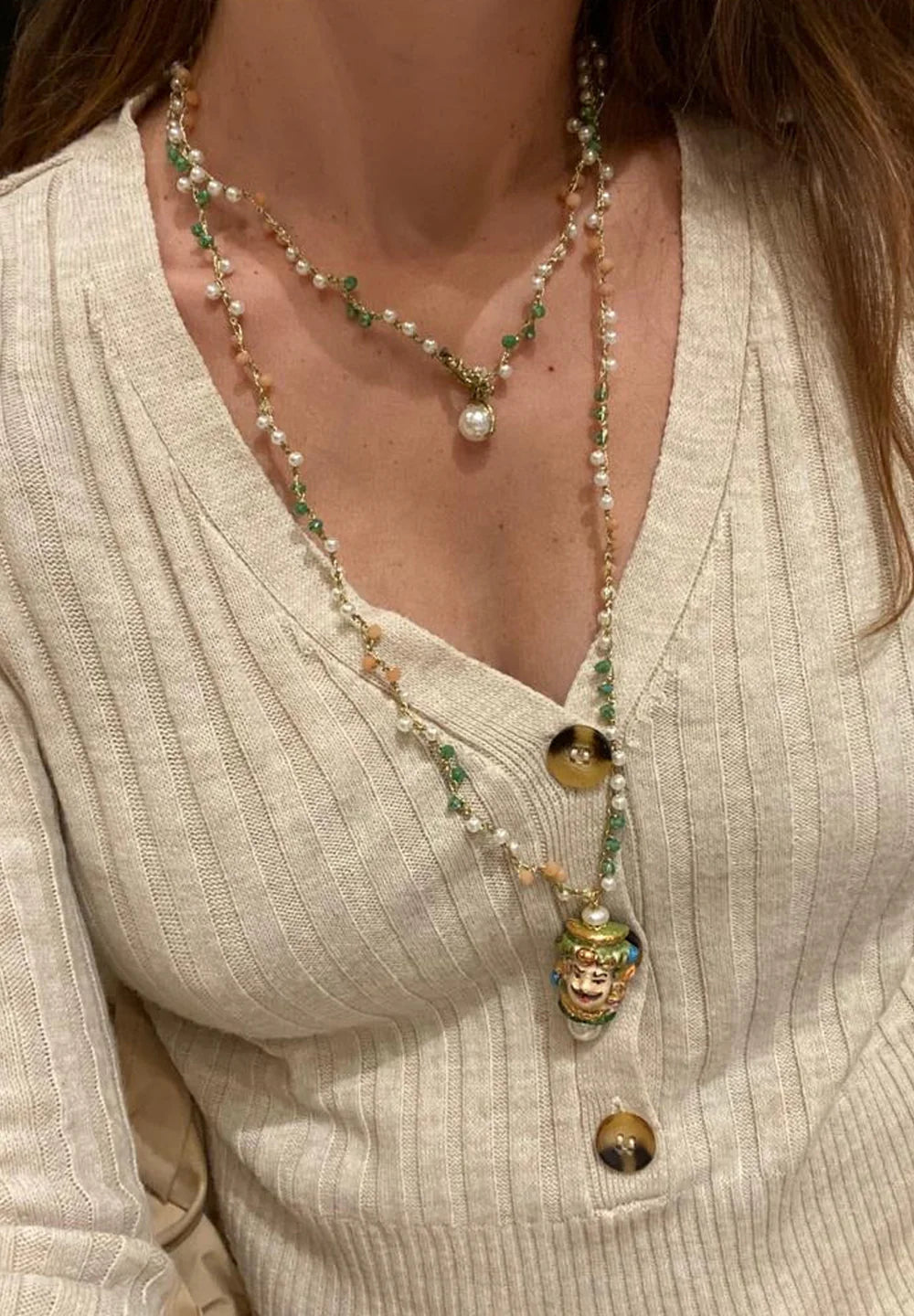Collar largo doble con cuentas verde oliva, detalles en dorado y colgante de cerámica de cabeza masculina siciliana pintada a mano. Combinado con jersey beige de cuello en pico.
