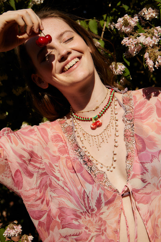 Collar de cuentas rojas y verdes con colgante de cerámica en forma de cerezas, sobre modelo. Cashfana.