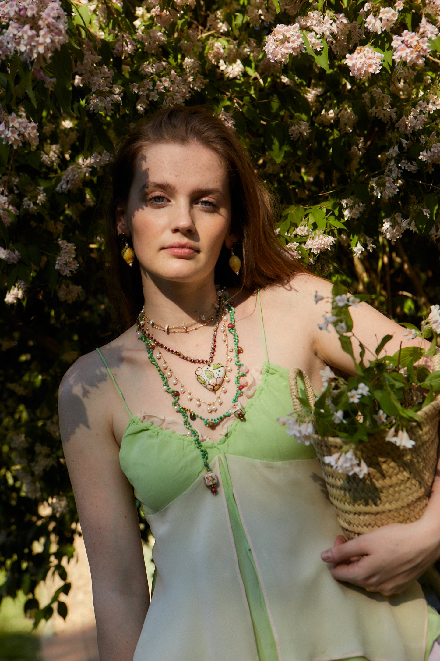 Modelo al aire libre con vestido verde claro luciendo el collar Corazoncito de cerámica pintado a mano de Cashfana, rodeada de flores.