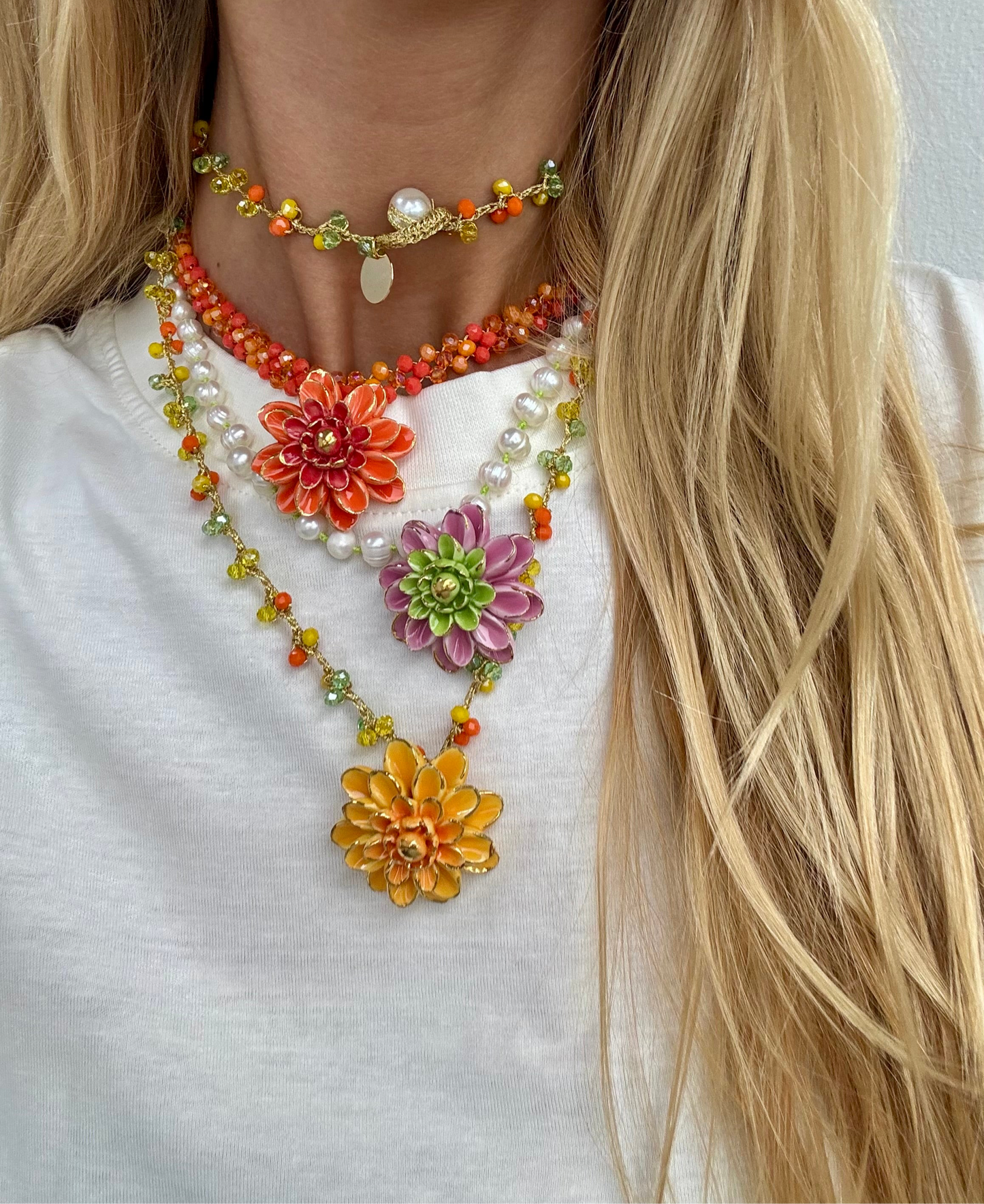 Collar de perlas blancas con colgante central de flor esmaltada en rosa y verde lima, sobre fondo camiseta blanca. Combinado con nuestro collar Sofía y Alice. Cashfana.