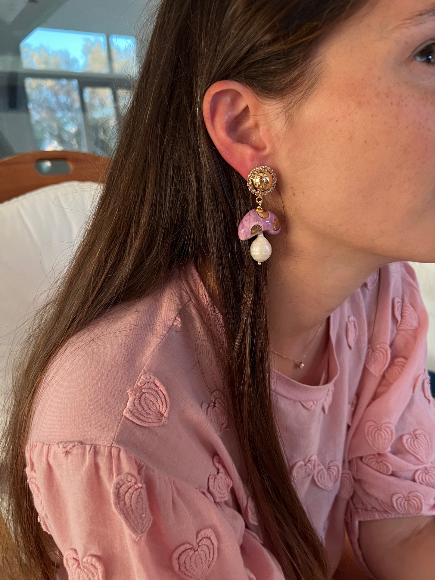 Pendientes con forma de setas lila con lunares dorados, cristales brillantes y perlas colgantes. Combinados con blusa osa con estampado de flores.