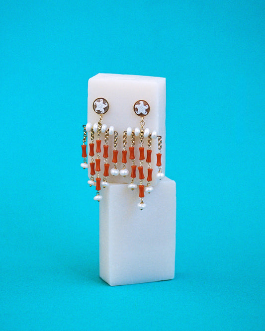 Pendientes largos con camafeo de estrella, coral natural y perlas. Sofisticación con esencia marina. Sobre esponjas blancas con fondo azul.