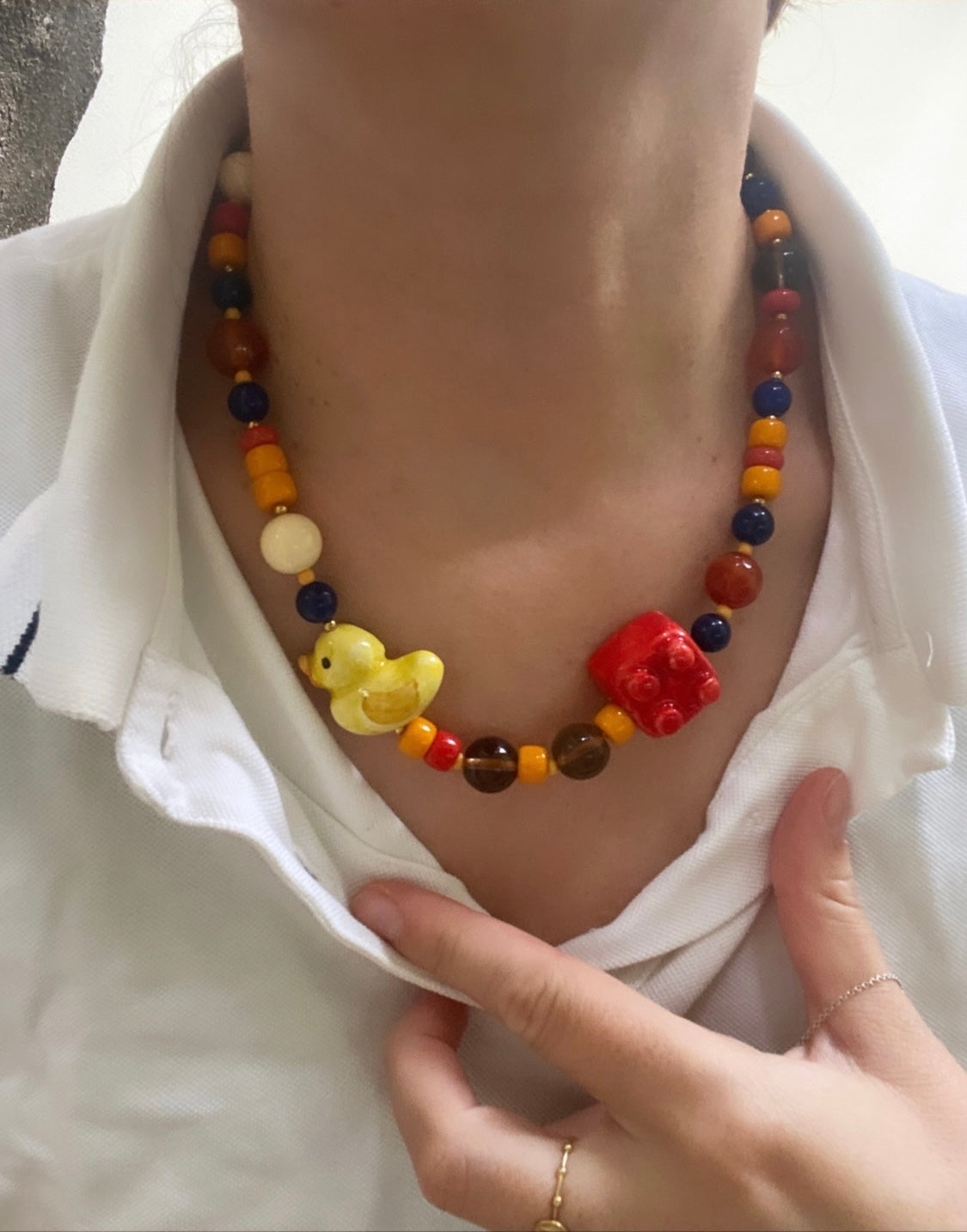 Collar con cuentas multicolor y charms de patito amarillo y bloque tipo LEGO rojo. Combinado con camisa blanca. Cashfana.