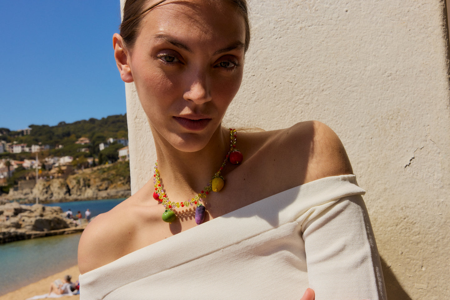 Collar de cuentas multicolor con cinco charms colgantes de cerámica: tomate rojo, manzana verde, berenjena morada, limón amarillo y otro tomate rojo, sobre modelo con blusa blanca con cuello dama de honor. Cierre con perla.