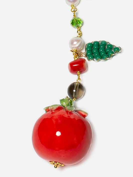 Colgante de cerámica en forma de tomate rojo, detalles de hojas y flores de cristal, sobre fondo blanco. Cashfana.