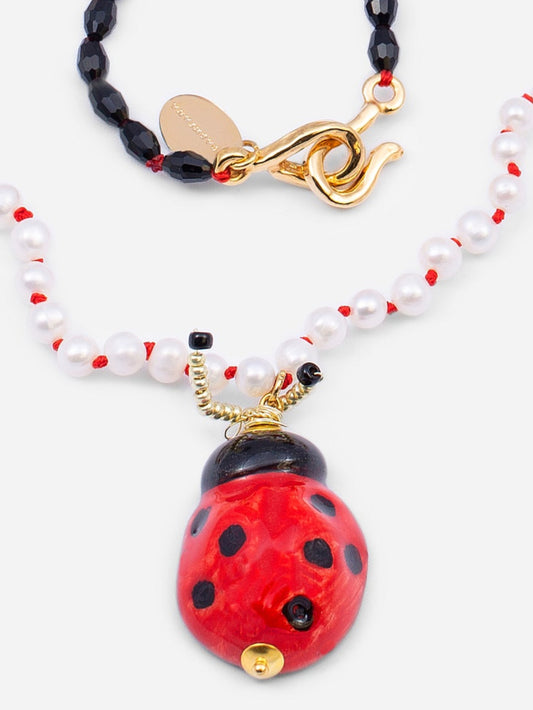 Collar con cuentas negras, rojas y doradas, y perlas intercaladas por nudos de hilo rojo, con colgantes de mariquita uno de cerámica esmaltada y otro de cuentas. Cashfana.