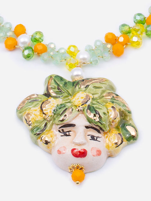 Collar corto con carita de cerámica esmaltada a mano, montado con cuentas naranjas y verdes en forma de flor y cristales. Cierre de broche con perla artificial. Cashfana.