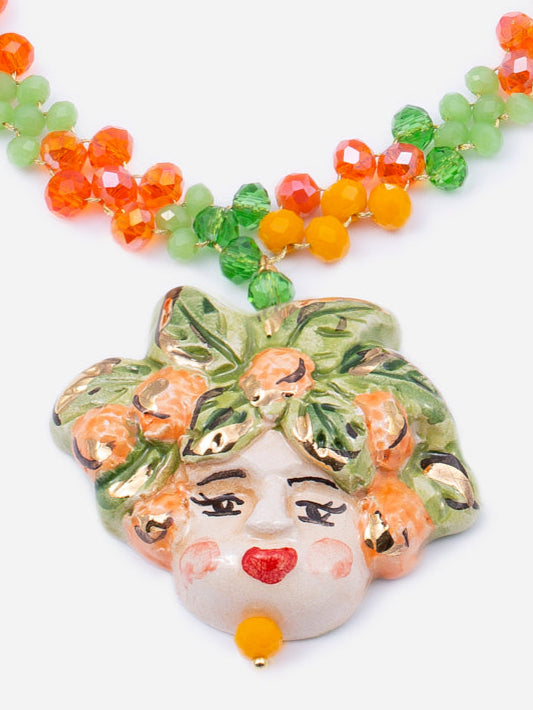 Collar corto con cuentas rojas, naranjas y verdes, y colgante de cerámica con rostro femenino entre hojas y frutas. Diseño artesanal de Cashfana.