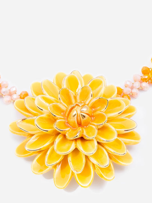 Collar carolina corto con cuentas rosadas y amarillas, decorado con una gran flor central de pétalos esmaltados en tonos amarillo y naranja, fondo blanco. Cashfana.