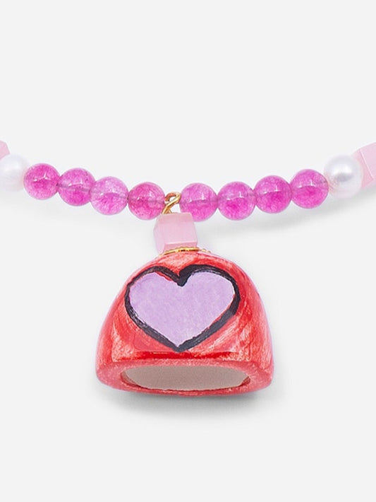 Colgante de cerámica en forma de campana roja decorada con corazón rosa, sobre fondo blanco. Cashfana.