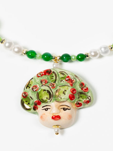 Collar corto con cuentas verdes, perlas y colgante de cerámica pintado a mano con una carita adornada de hojas y uvas rojas. Cierre dorado con extensión.