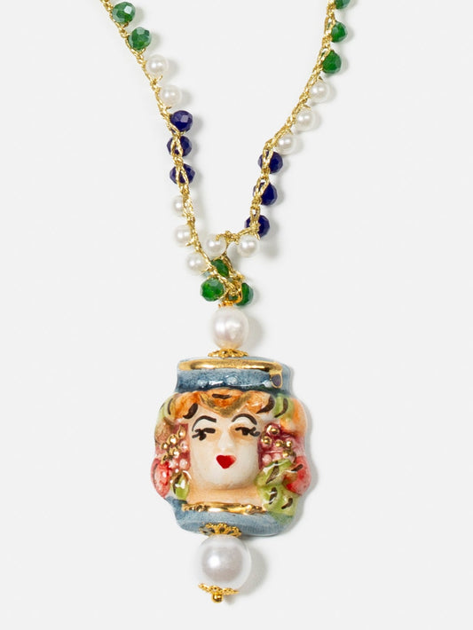 Collar largo con cuentas verdes, azul marino y perlas pequeñas, cierre dorado con perla y colgante de cerámica de rostro femenino pintado a mano.