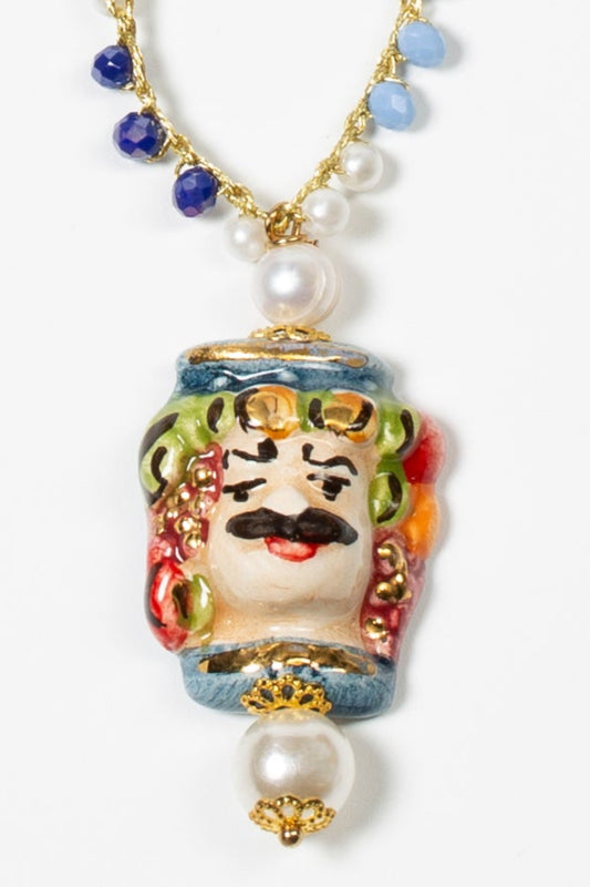 Collar largo con cuentas en azul y blanco, cierre dorado con perla y colgante de cerámica esmaltada con rostro masculino pintado a mano. Cashfana.