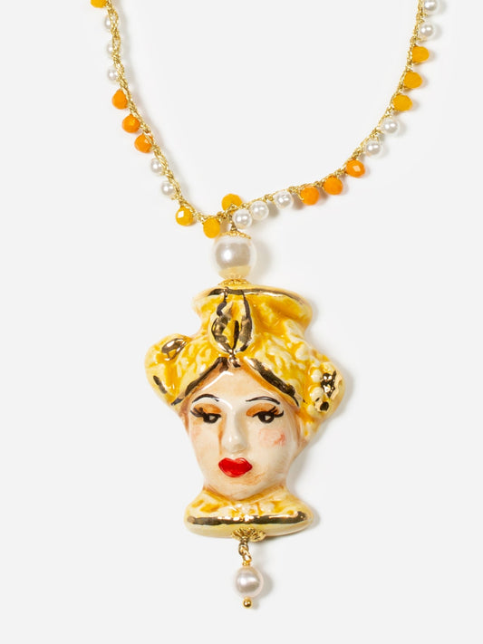 Collar largo con cuentas color miel y perlas naturales, con colgante de cerámica pintado a mano con rostro femenino y detalles dorados. Cashfana.