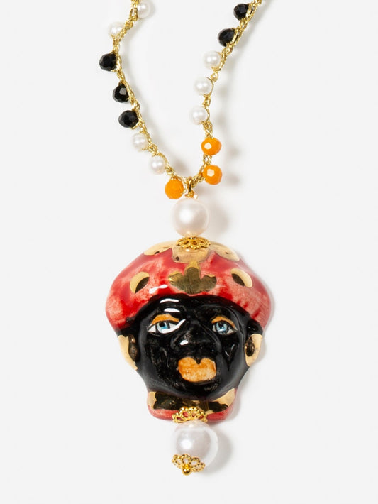 Collar largo con cuentas negras, naranjas y perlas pequeñas, cierre dorado con perla y colgante de cerámica con rostro masculino pintado a mano.