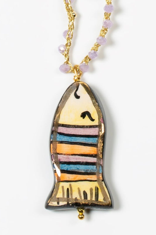 Detalle de collar mini pez lila con cuerda de crochet dorada y cuentas de cristal azules sobre fondo blanco. Cashfana