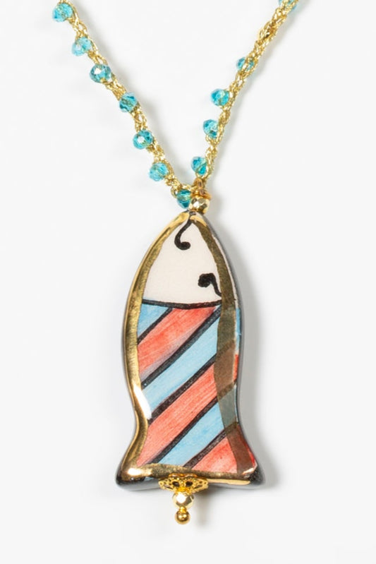 Detalle de collar mini pez azul con cuerda de crochet dorada y cuentas de cristal azules sobre fondo blanco. Cashfana.