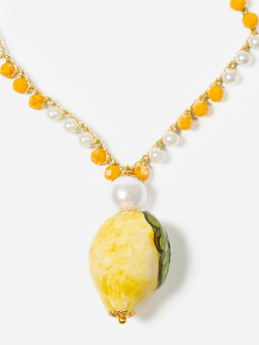 Collar largo con cuentas en tonos cítricos y colgante esmaltado en forma de limón degradado y cierre de perla. Cashfana.