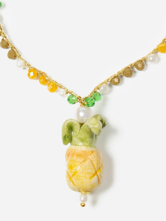 Collar de cuentas amarillas, verdes, blancas y marrones con colgante de cerámica en forma de banana, sobre fondo blanco. Cashfana.