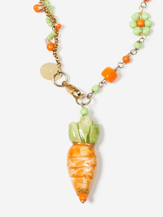 Collar largo con cuentas verdes y naranjas, con colgante de cerámica en forma de zanahoria, sobre fondo blanco.
Cashfana.