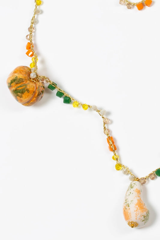 Collar largo con cuentas en tonos naranja y verde, charms de cerámica en forma de calabazas, sobre fondo blanco.
Cashfana.