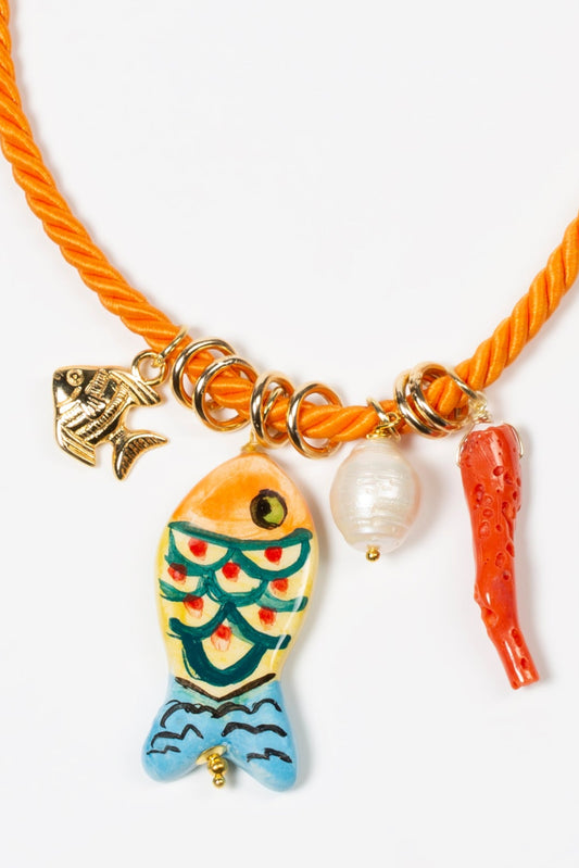 Detalle de collar de cordón con cerámica en forma de pez colgando junto con un coral sobre fondo blanco. Cashfana.