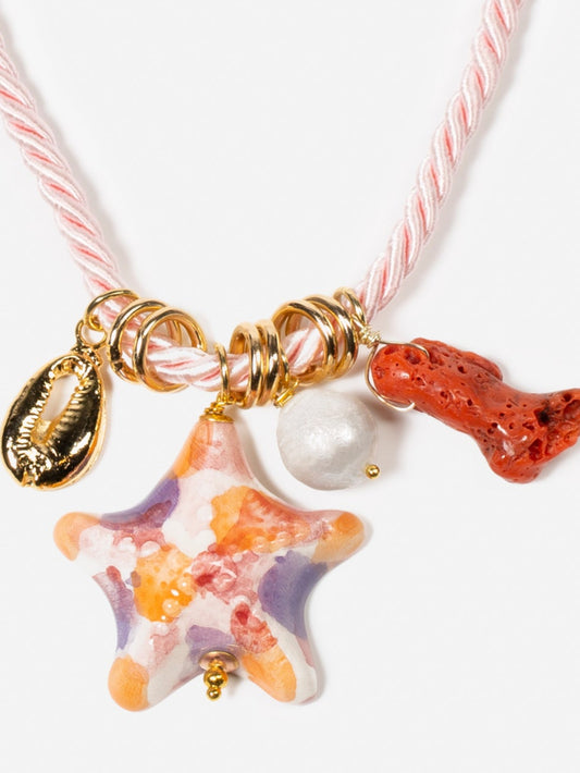 Detalle de collar estrella de mar rosa cordón rosa satinado sobre fondo blanco, con coral y concha dorada. Cashfana