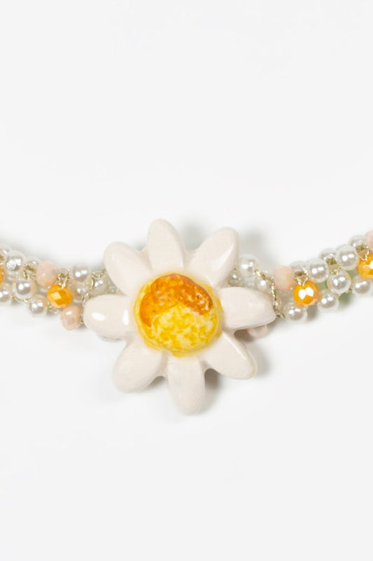 Choker corto con doble hilera de perlas, cuentas en tonos verde lima, naranja suave y dorado, con margarita esmaltada en blanco y centro amarillo brillante, sobre fondo blanco. Cashfana.