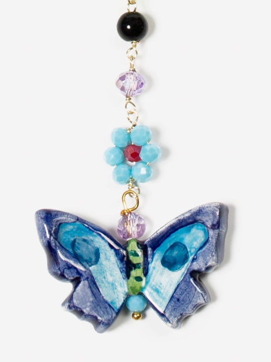 Collar largo con cuentas de colores en forma de flores y mariposa azul como dije central. Fondo blanco. Cashfana.