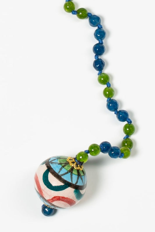Collar largo con cuentas azul y verde, cierre dorado, perlas barrocas naturales y colgante cerámico pintado a mano en forma de cápsula decorativa.