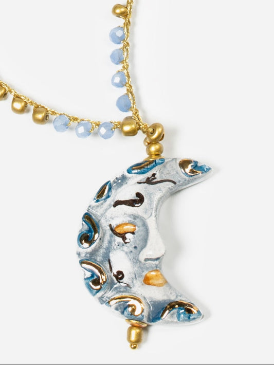 Colgante en forma de luna creciente de cerámica esmaltada en blanco perlado, gris azulado y detalles dorados sobre fondo blanco. Cashfana.