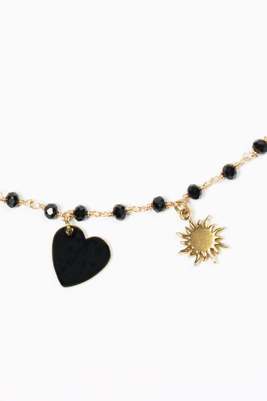 cadena dorada con cuentas negras, charm de corazón negro y sol dorado.