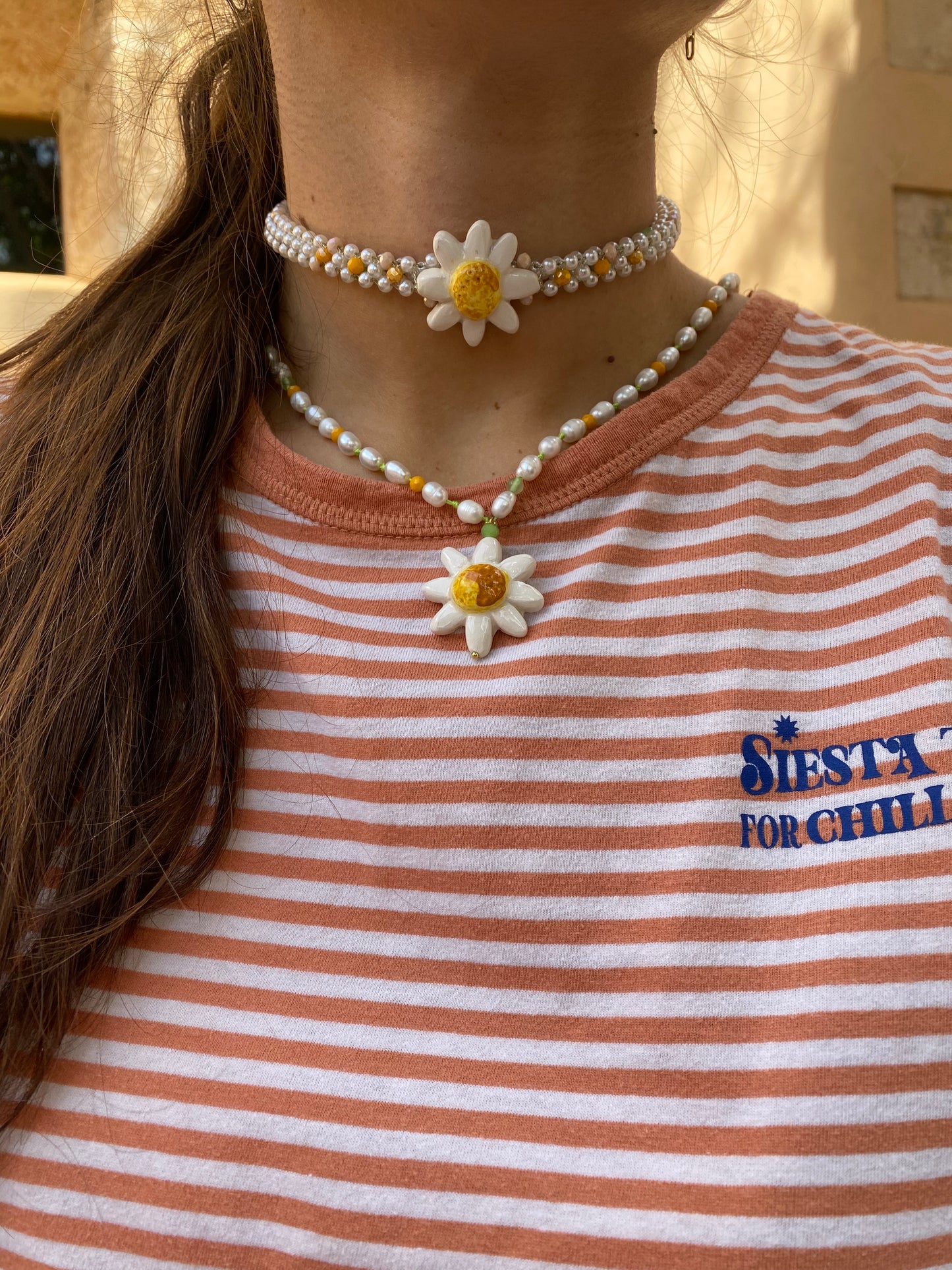 Choker corto con doble hilera de perlas, cuentas en tonos verde lima, naranja suave y dorado, con margarita esmaltada en blanco y centro amarillo brillante, sobre camiseta de rayas combinado con el collar The One. Cashfana.