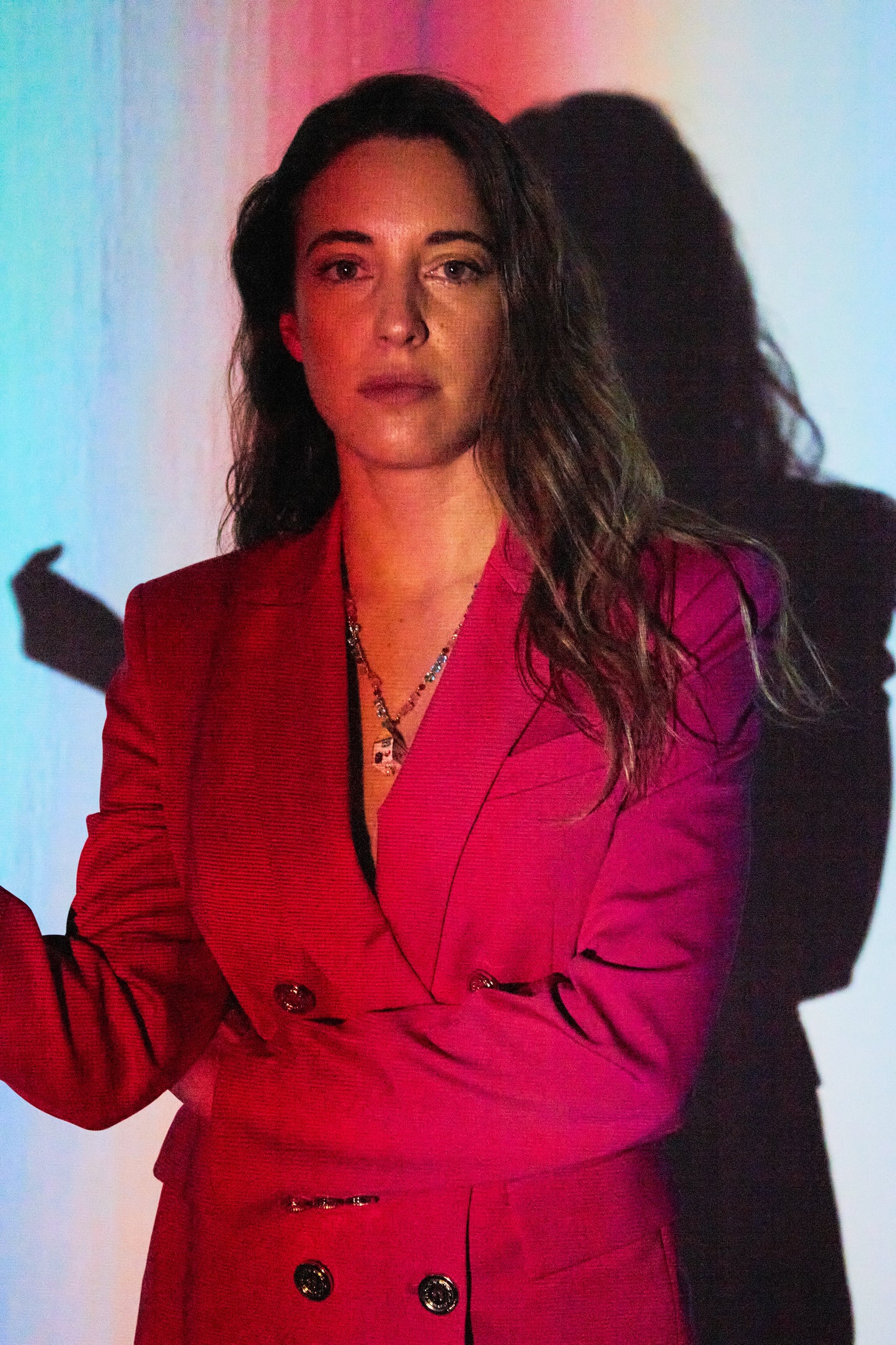 Modelo con americana roja y luces con collar largo con cuentas rosas, verdes y blancas y colgante de cerámica pintado a mano en forma de casa, sobre fondo blanco. Cashfana.