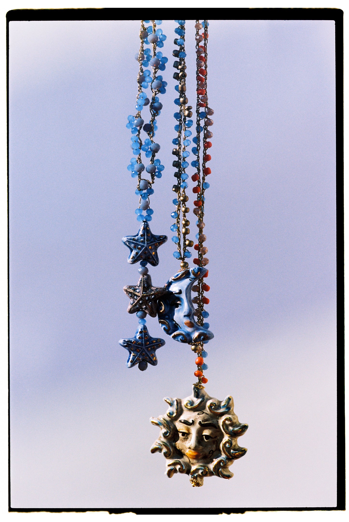 Collar de largo medio con cuentas en tonos azul cielo, blanco traslúcido y marfil, decorado con tres estrellas de cerámica pintadas a mano en azul pastel, blanco con puntos oscuros y azul hielo. Piccolle Stelle. Colgando con el collar luna y sole. Cashfana.