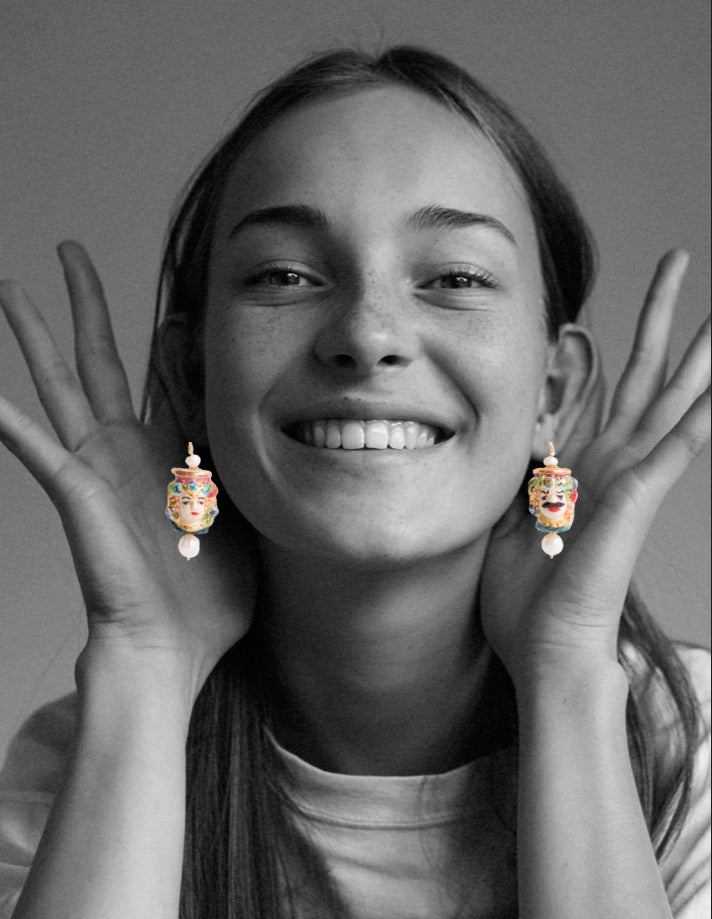 Pendientes esmaltados con bustos sicilianos masculino y femenino, detalles florales y perla colgante. En collage en blanco y negro con modelo sonriente.