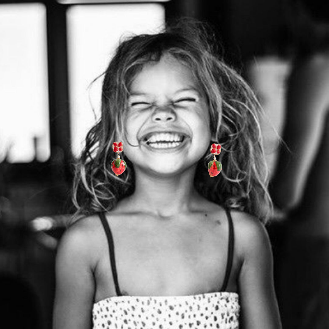 Pendientes con cristal rojo y colgante en forma de fresa de cerámica pintada a mano. Sobre collage en blanco y negro con niña sonriente.