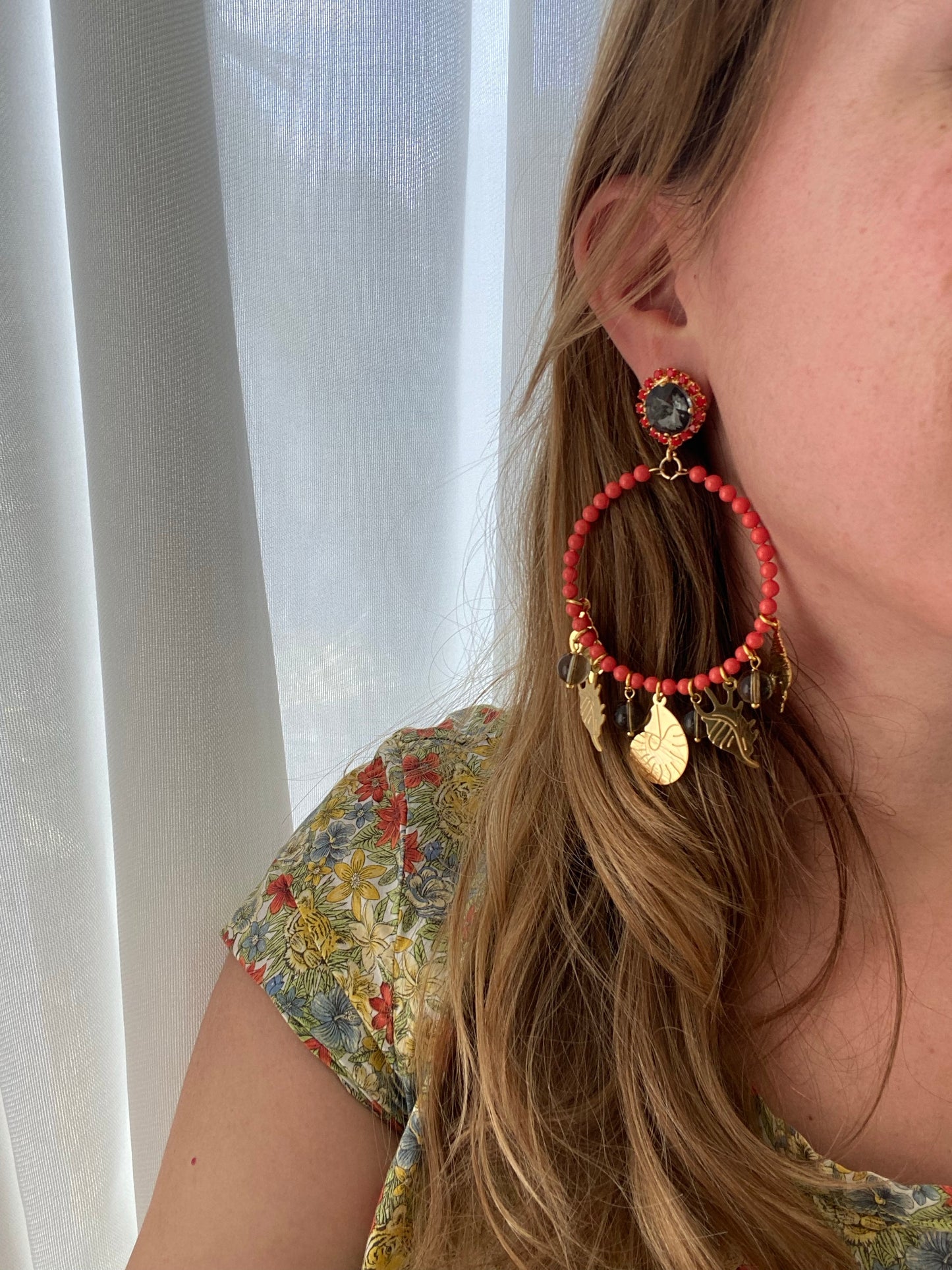 Pendientes de aro coralino con colgantes dorados marinos y piedra negra central rodeada de cuentas rojas. Combinados con blusa floral.