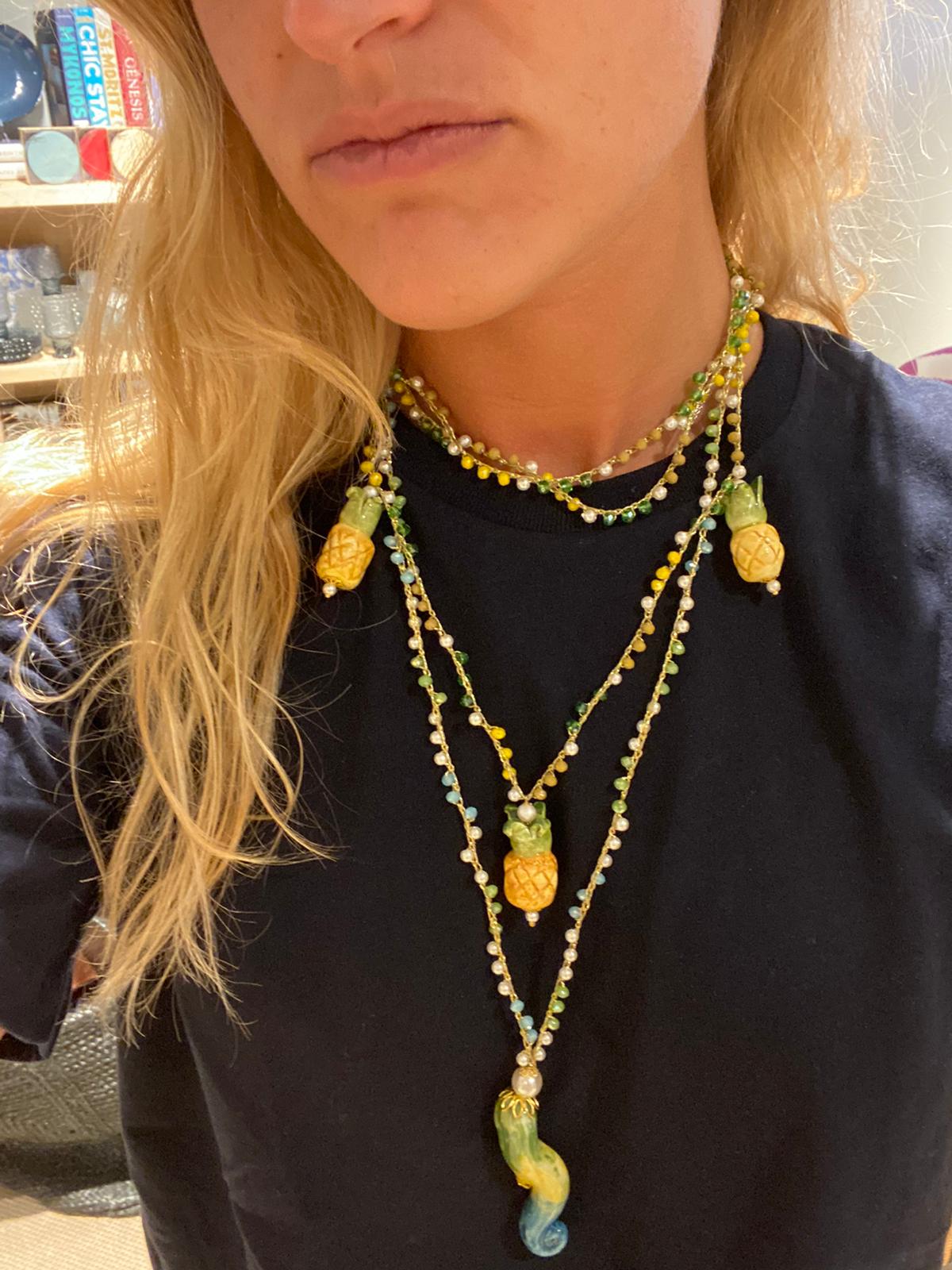 Collar de cuentas amarillas, verdes, blancas y marrones con colgante de cerámica en forma de banana, sobre camiseta negra. Cashfana.