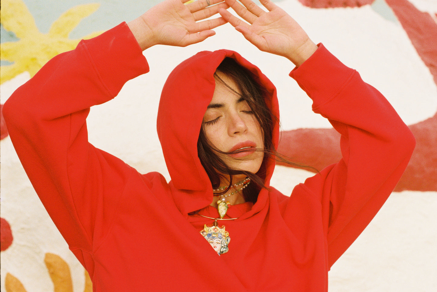 Collar rígido dorado con colgante de busto femenino siciliano en cerámica pintada a mano con detalles florales y perla decorativa. Conjuntado con sudadera roja.