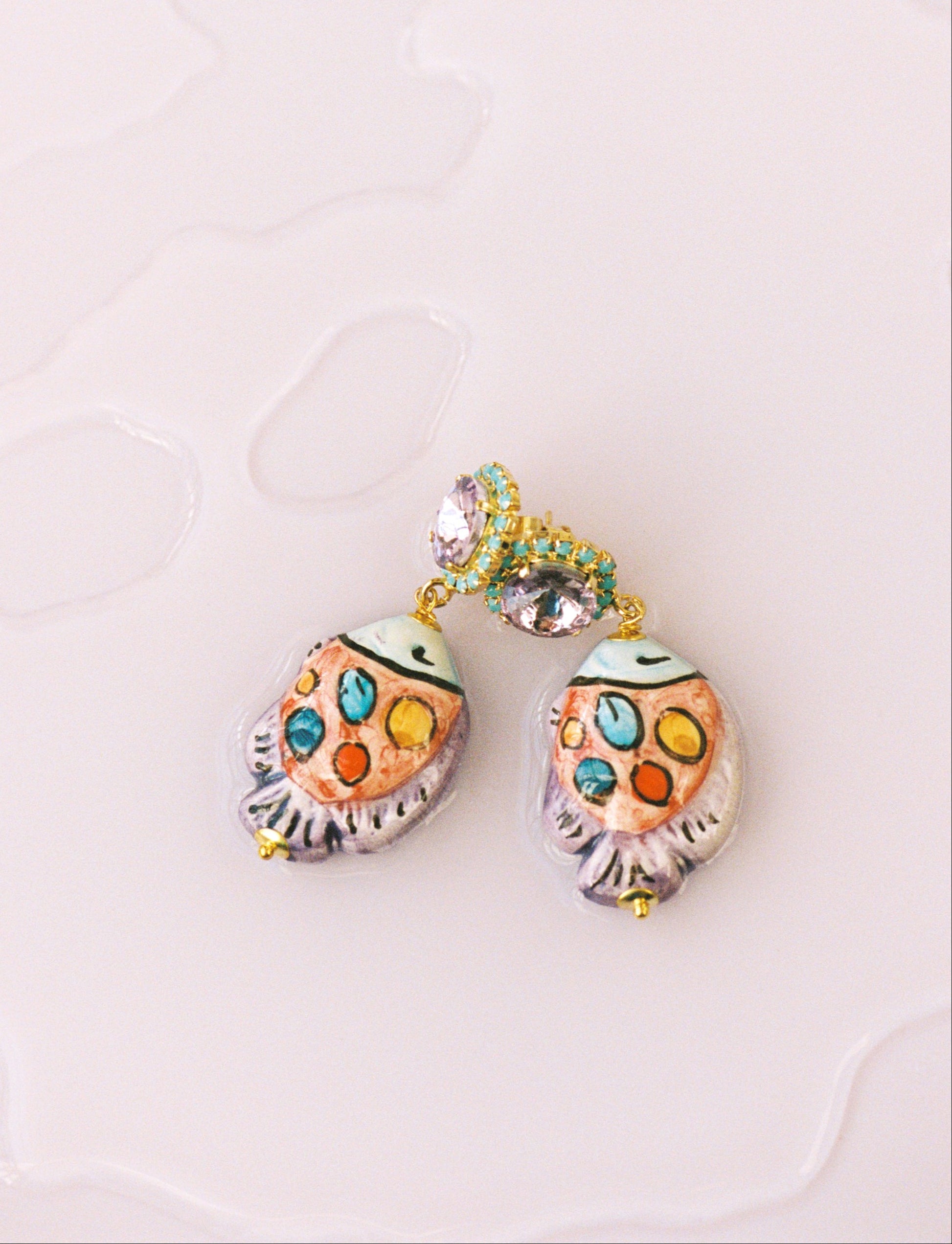Pendientes pececito de cerámica esmaltada pintados a mano, con base de cristal lavanda y detalles en colores vivos.
Sobre fondo de agua.