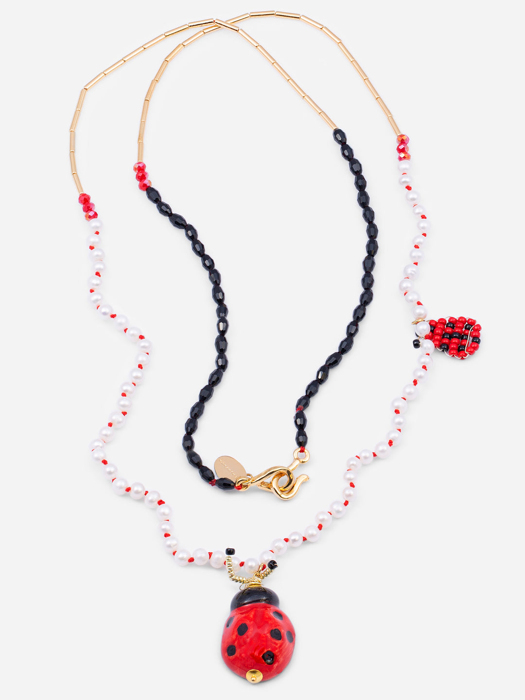 Collar con cuentas negras,  rojas y doradas, y perlas intercaladas por nudos de hilo rojo, con colgantes de mariquita uno de cerámica esmaltada y otro de cuentas. Cashfana.

