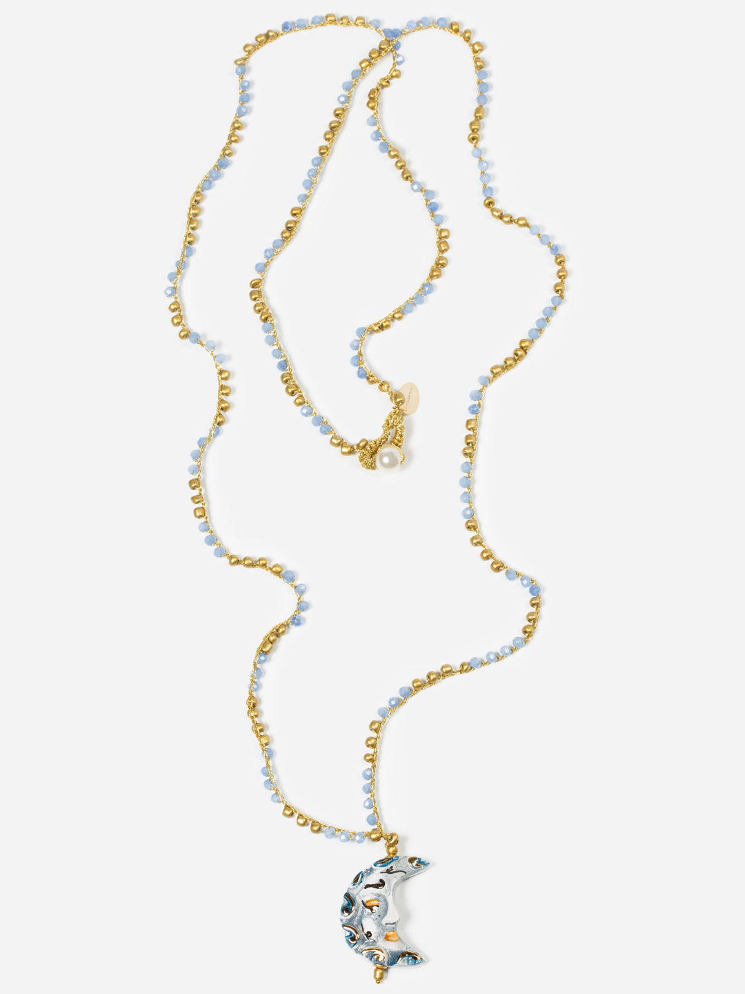 Collar largo de cuentas azul celeste y doradas con colgante en forma de luna creciente de cerámica esmaltada en blanco perlado, gris azulado y detalles dorados sobre fondo blanco. Cashfana.